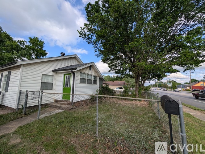 A small house with a green door is surrounded by a fence and has a mailbox in front.