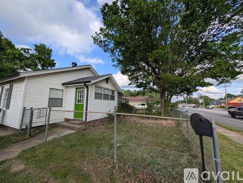 A small house with a green door is surrounded by a fence and has a mailbox in front.