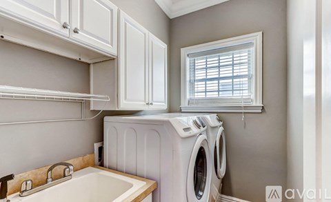 A white washing machine is in a laundry room with a window.