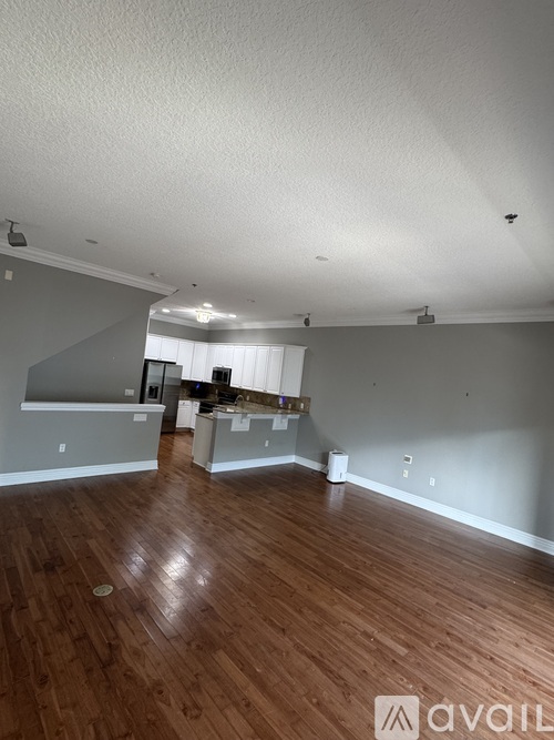 A large empty room with wooden floors and a kitchen area in the background.