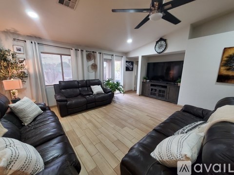 A living room with black leather couches and a ceiling fan.
