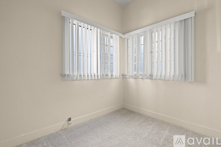 A room with a carpeted floor and a window with white blinds.