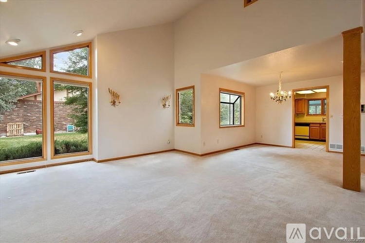 A spacious living room with a chandelier and a view of a backyard through the windows.