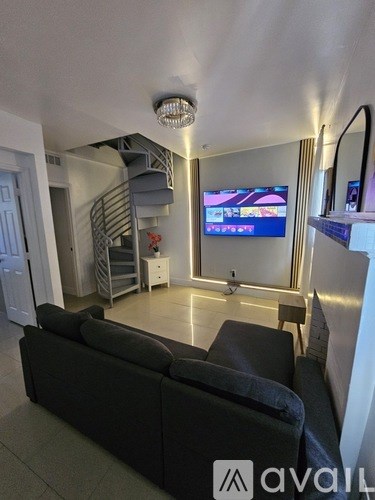 A living room with a black couch and a television on the wall.