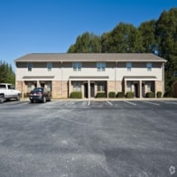 A parking lot in front of a building with a white car and black car parked.