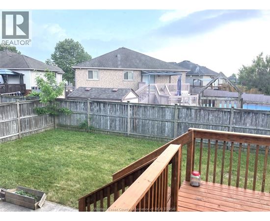 A wooden deck overlooks a backyard with a pool and houses in the background.