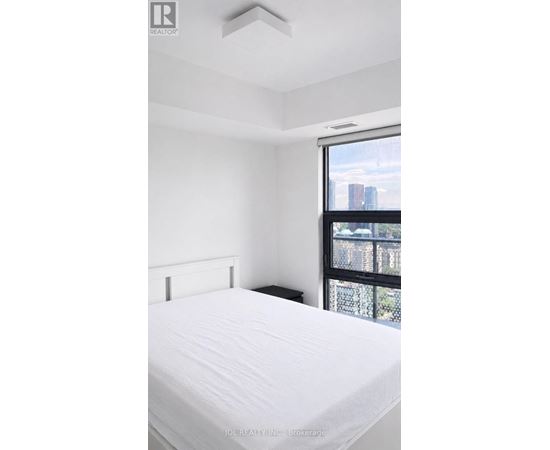 A white bed in a room with a window overlooking a cityscape.