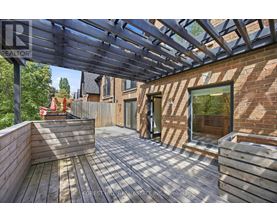 A wooden deck with a pergola and a brick building in the background.