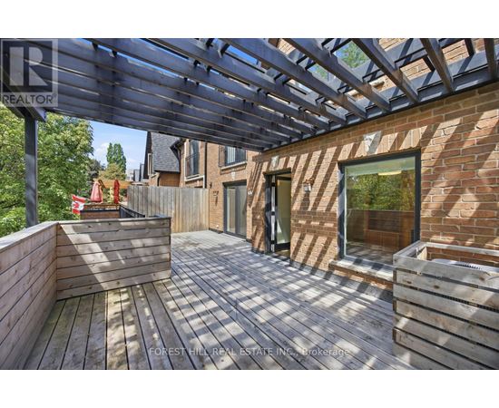 A wooden deck with a pergola and a brick building in the background.