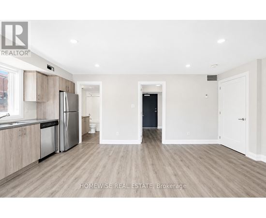 A spacious kitchen and living room with a refrigerator, sink, and a doorway leading to another room.