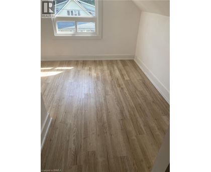 A room with light wood flooring and a window showing a house outside.