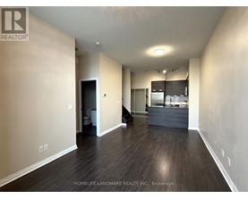 A spacious room with wooden floors and a kitchen area in the background.