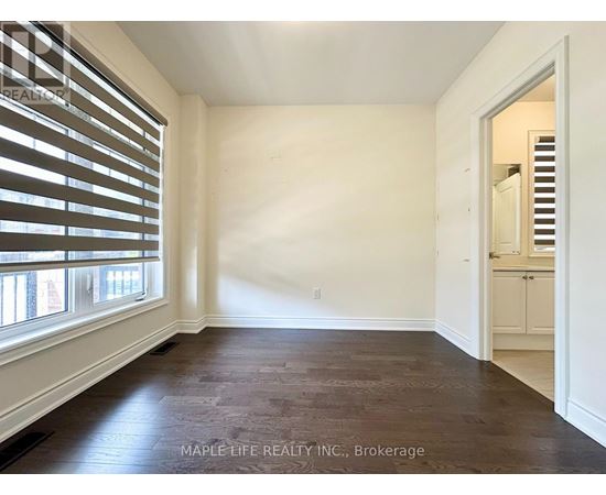 A room with wooden floors and white walls, with a doorway leading to another room.