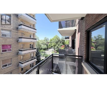 A balcony overlooks a tree-lined street from a brick building.