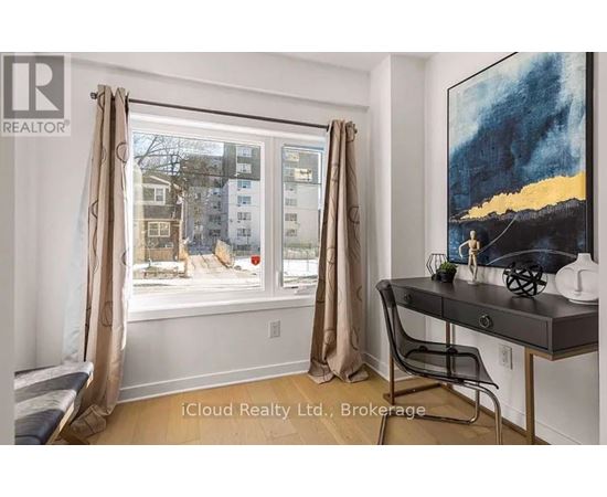 A room with a desk and a window showing an apartment building outside.
