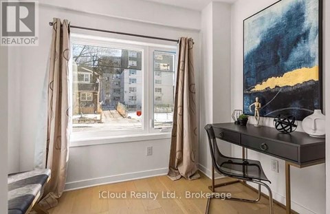 A room with a desk and a window showing an apartment building outside.