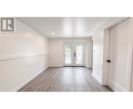 A room with white walls and a wooden floor with a door leading outside.