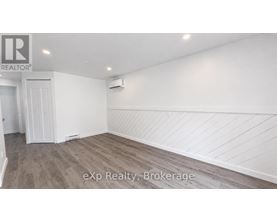 A room with white walls and wooden flooring, with a door on the left and a wall-mounted air conditioner on the right.
