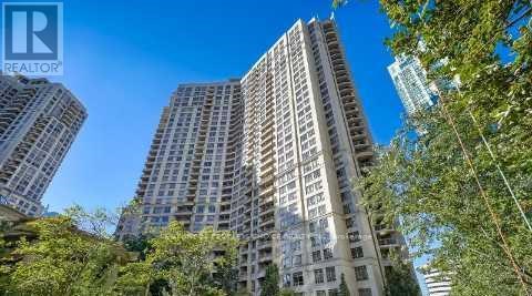 A tall residential building with a clear blue sky above and trees in the foreground.