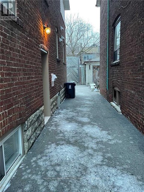 A narrow alley with a brick wall and a metal trash can.