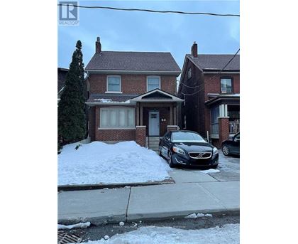 A black car is parked in front of a house with a snow bank.