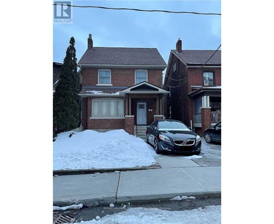 A black car is parked in front of a house with a snow bank.