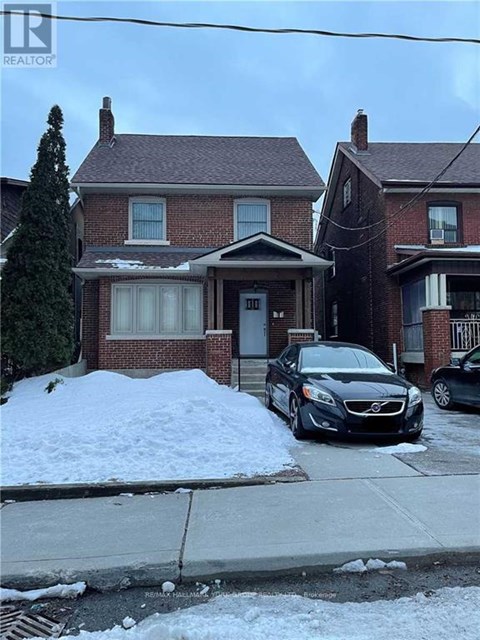 A black car is parked in front of a house with a snow bank.