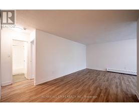 A room with wooden flooring and white walls, with a doorway leading to another room.