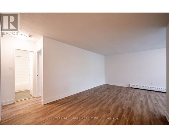 A room with wooden flooring and white walls, with a doorway leading to another room.