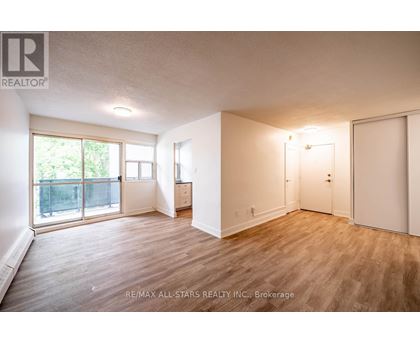 A spacious room with wooden flooring and white walls, furnished with a desk and a chair.
