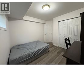 A bedroom with a bed covered in a grey sheet, a wooden desk, and a white door.