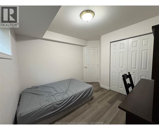 A bedroom with a bed covered in a grey sheet, a wooden desk, and a white door.
