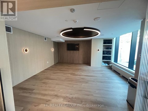 A spacious room with wooden flooring and a large window on the right side.