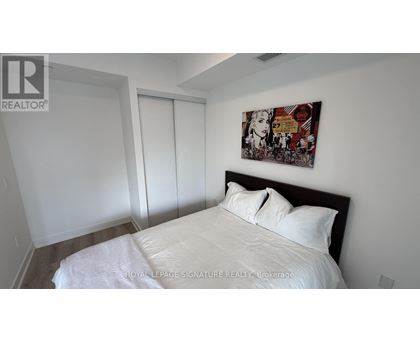 A bedroom with a bed, a painting on the wall, and a sliding door.
