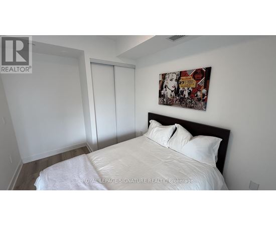 A bedroom with a bed, a painting on the wall, and a sliding door.