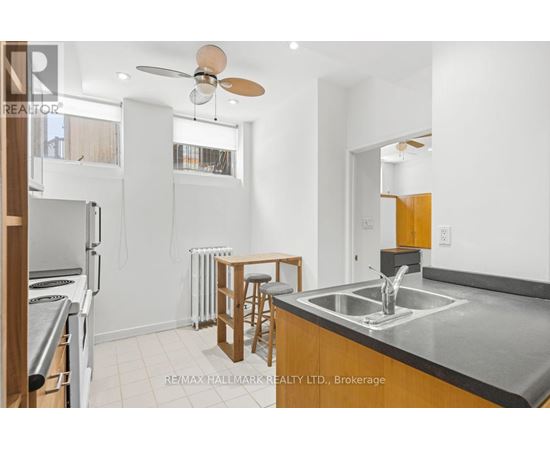 A kitchen with a stove top oven, a bar stool, and a fan.