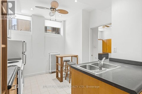 A kitchen with a stove top oven, a bar stool, and a fan.