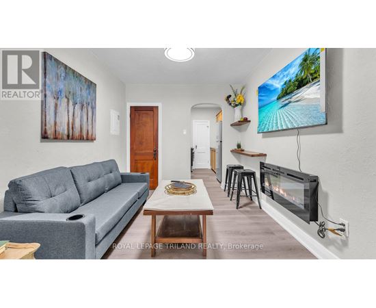 A living room with a grey couch and a painting of trees on the wall.