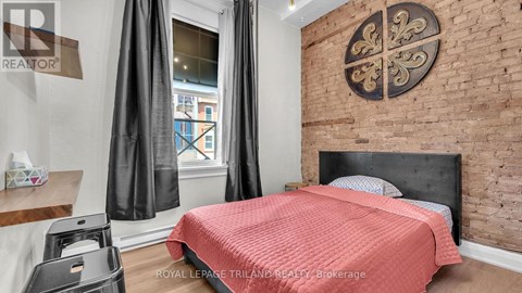 A bedroom with a red bedspread and a brick wall with a decorative plate.