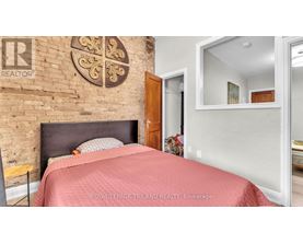 A bedroom with a brick wall and a bed with a red bedspread.