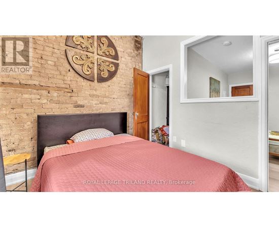 A bedroom with a brick wall and a bed with a red bedspread.