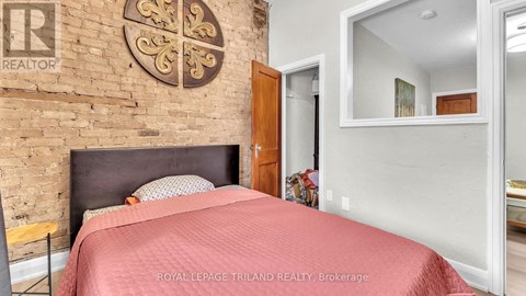 A bedroom with a brick wall and a bed with a red bedspread.