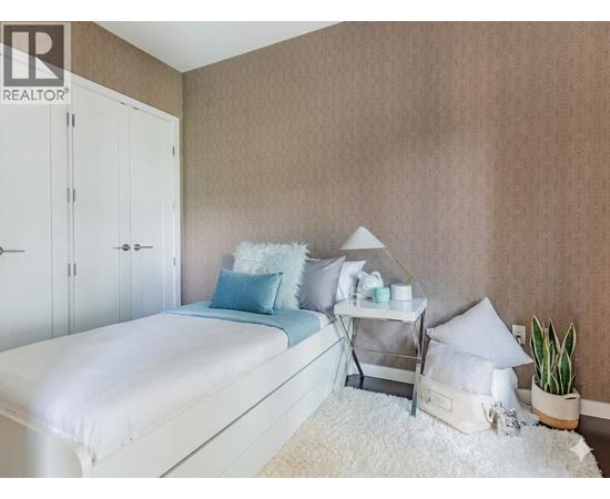 A bedroom with a white bed and a white nightstand with a plant on it.