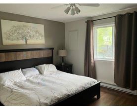 A bedroom with a bed, a ceiling fan, and a painting of a tree on the wall.