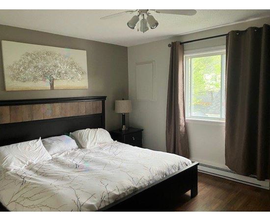 A bedroom with a bed, a ceiling fan, and a painting of a tree on the wall.