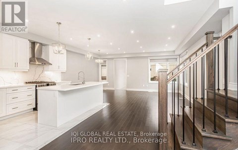 A spacious kitchen with white cabinets and a wooden staircase.
