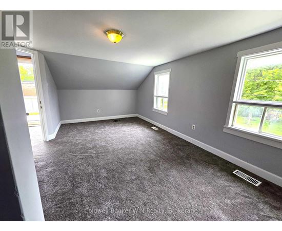 A room with grey carpeting and a window showing greenery outside.