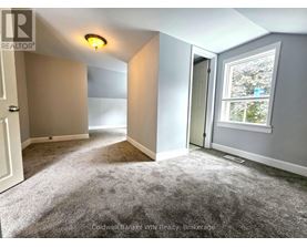 A room with a grey carpet and a window showing trees outside.