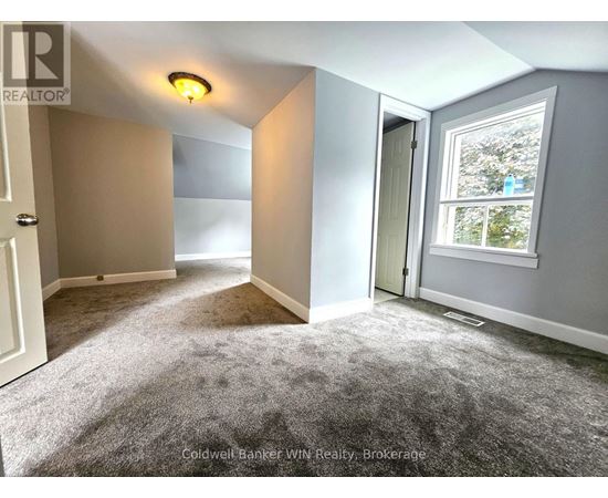 A room with a grey carpet and a window showing trees outside.