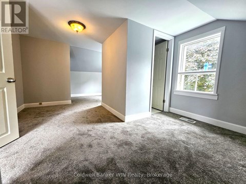A room with a grey carpet and a window showing trees outside.